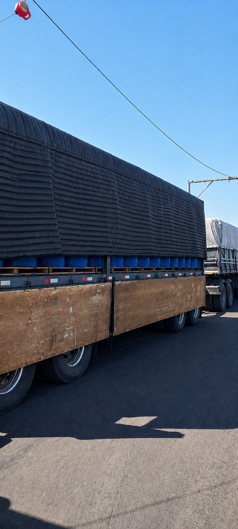 Lona térmica preta protegendo carga de tambores durante transporte rodoviário