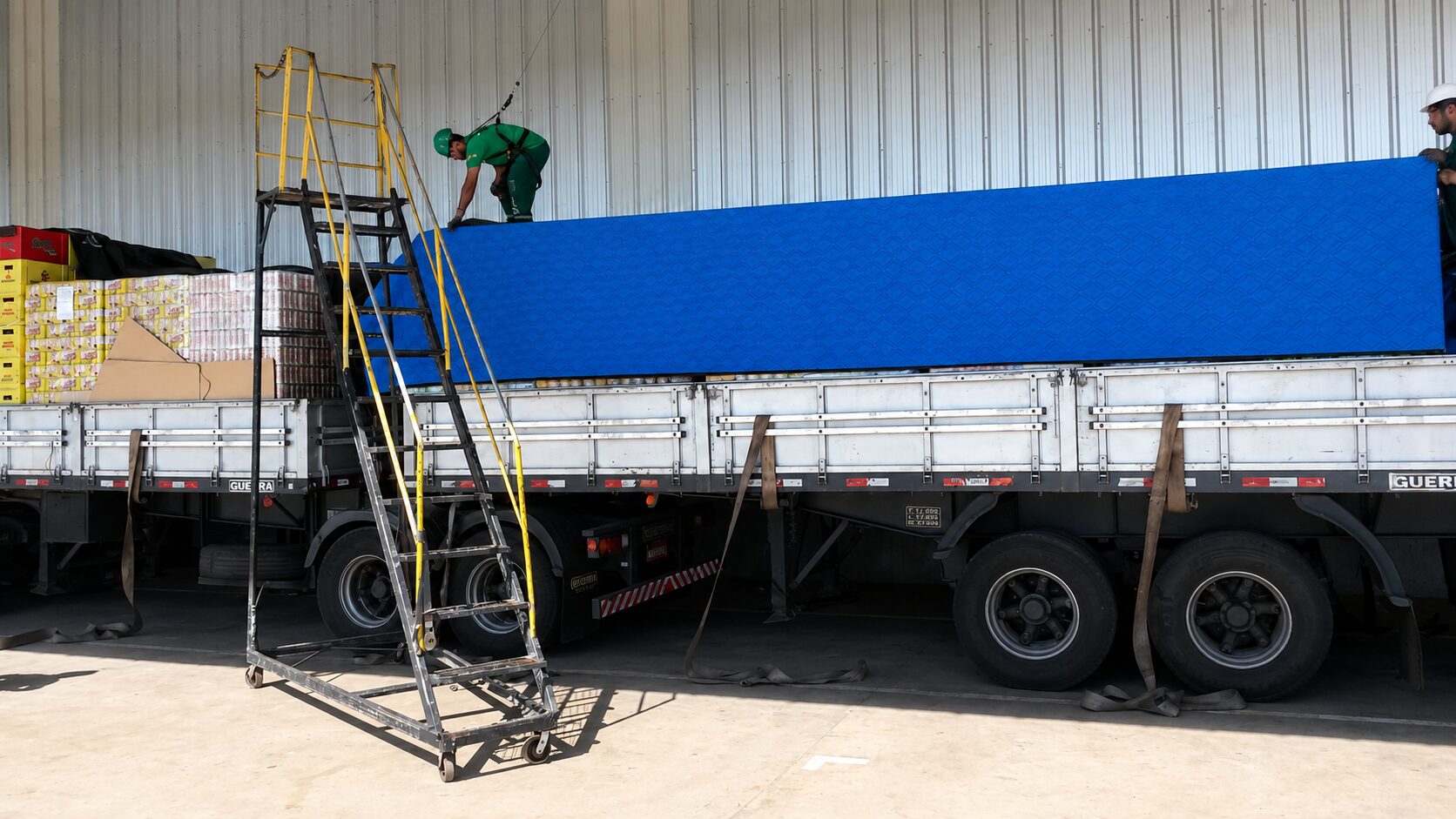 Equipe instalando lona térmica azul sobre carga paletizada em carreta